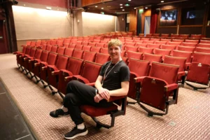 A person sitting in a red cinema seat within an empty auditorium.