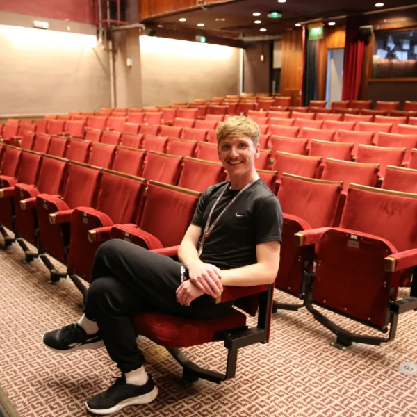 A person sitting in a red cinema seat within an empty auditorium.