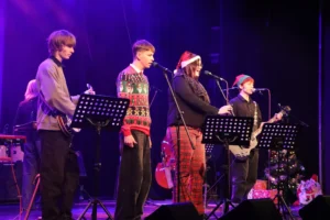 Four musicians on stage with music sheets performing for a Christmas event.
