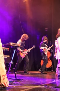 Musician playing guitar on stage with guitarist and cellist