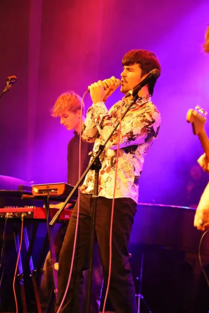 Man playing guitar on stage with purple lighting.