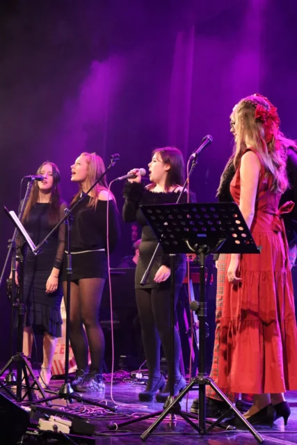 four women on stage singing with music stand