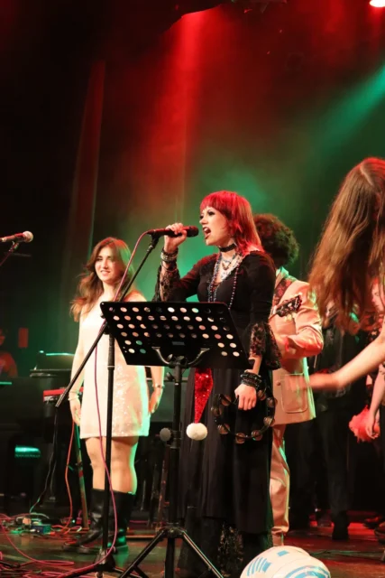 A group of people performing on stage with music sheets and microphones.