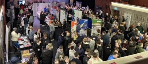 A crowded event space with people standing and talking, with posters on display.