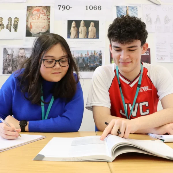Two students sitting at a table with an open book and papers, engaged in studying or working on a project.
