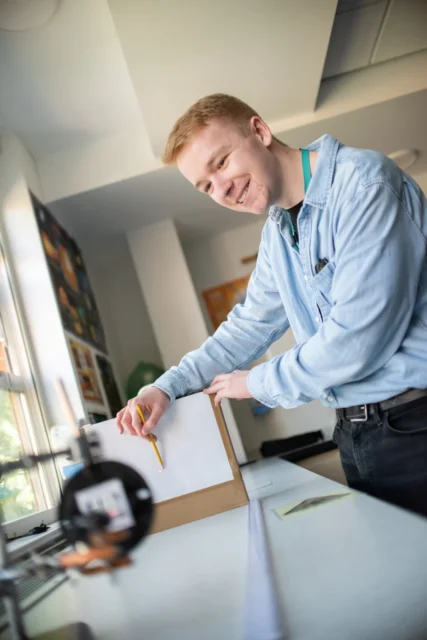 Young man smiling while working on a piece of paper on a table.