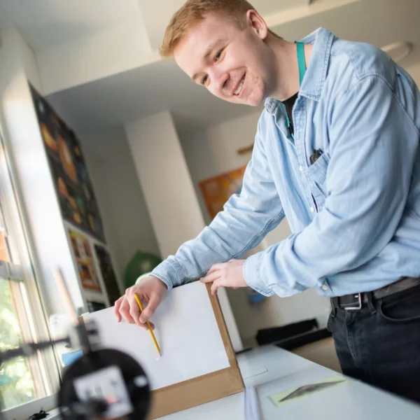 Young man smiling while working on a piece of paper on a table.