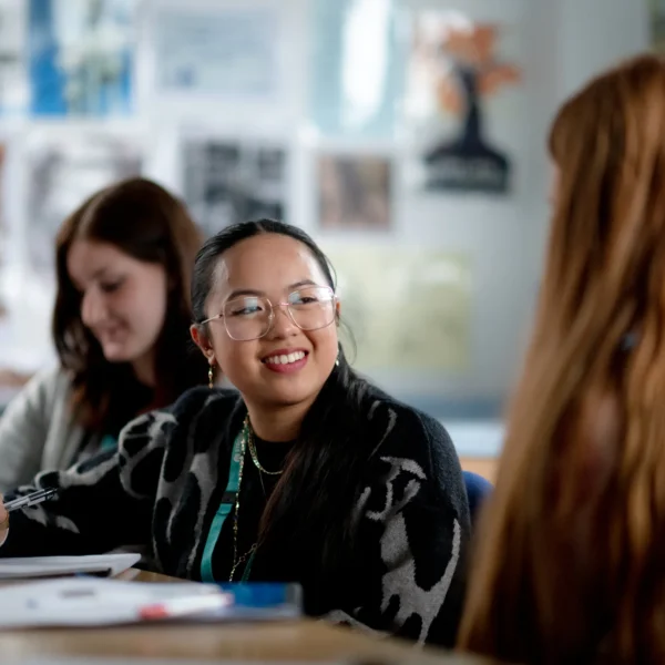Three people sitting at a table, two women and a girl, appear to be in a classroom setting