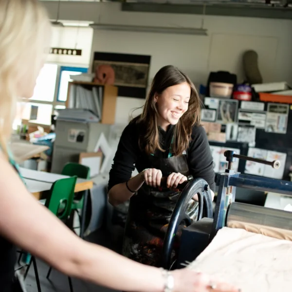 Two women working on a large piece of fabric in a workshop.