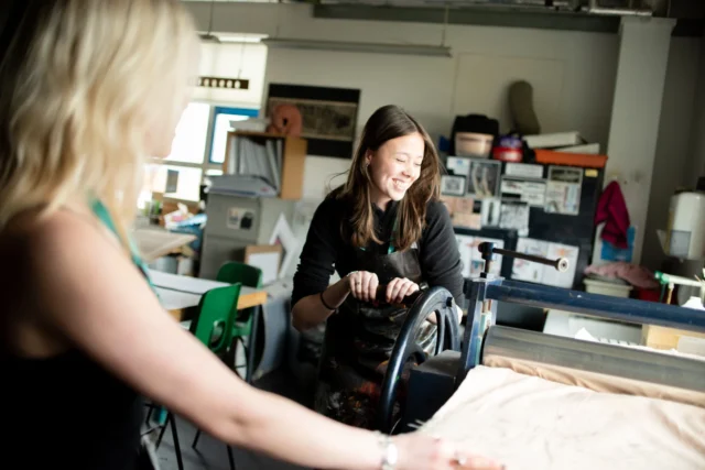 Two women working on a large piece of fabric in a workshop.