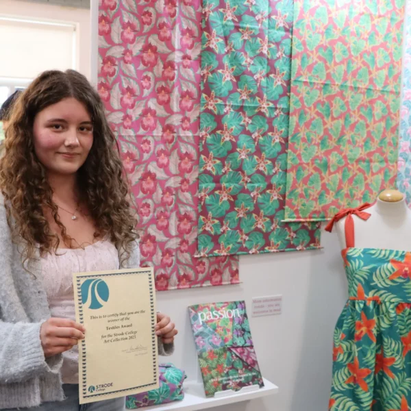 A young woman holding a certificate next to a mannequin with a dress.