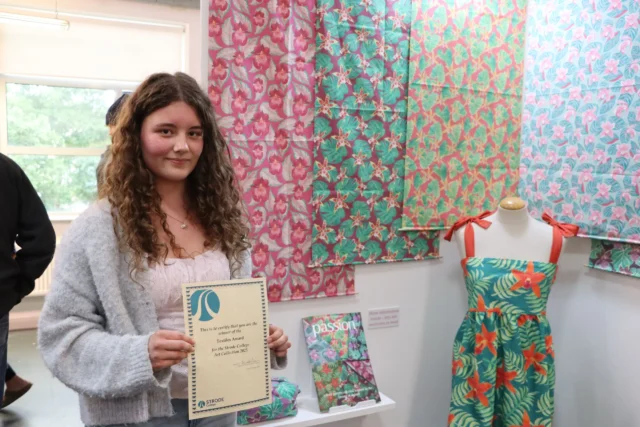 A young woman holding a certificate next to a mannequin with a dress.