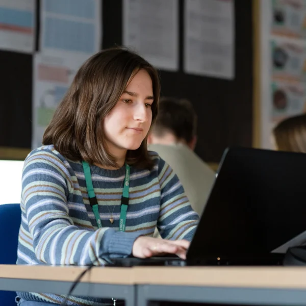A young girl with brown hair sitting at a desk with a laptop on it.