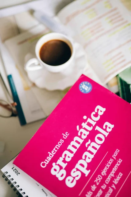 A Spanish grammar workbook with a cup of coffee on a desk.