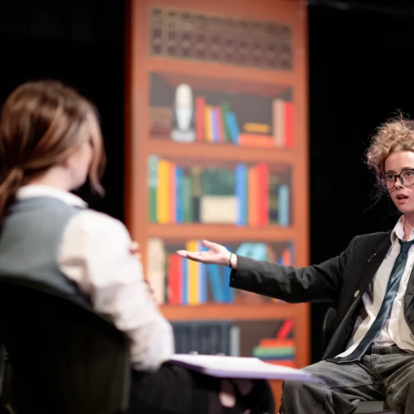 A man sitting in a chair gesturing while talking to two people across from him.