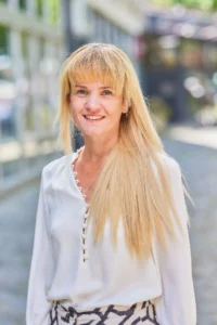 A woman with long blonde hair and bangs smiles at the camera.