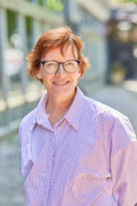 A woman with short red hair and glasses on a city street.