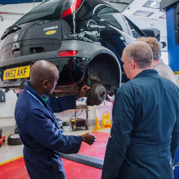 Two mechanics in blue overalls inspecting a car on a lift in a garage.