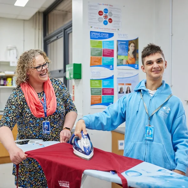 A woman and a boy ironing a red sheet in a classroom setting.