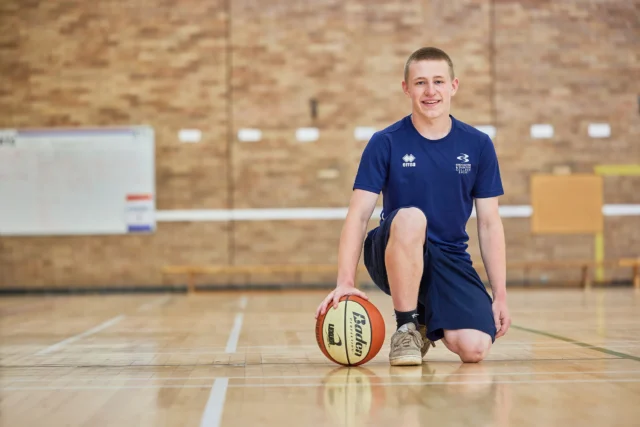 A man kneeling on a basketball court with a ball.