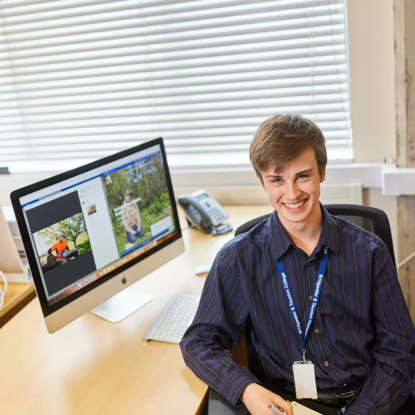 A young man sitting at a desk with a computer monitor displaying an image.