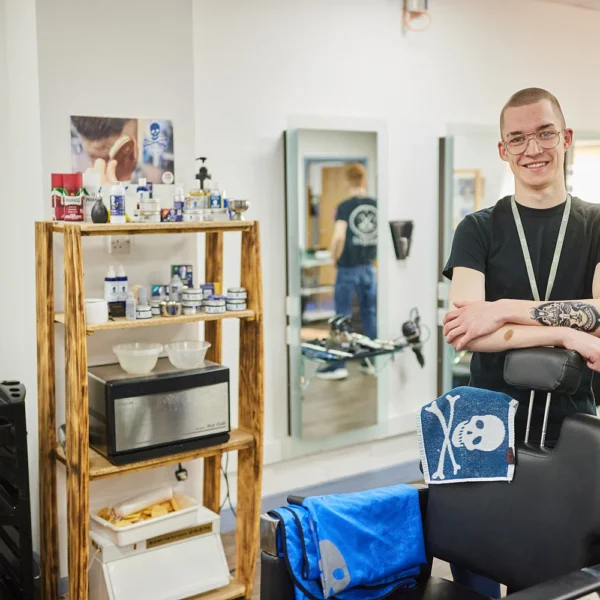 Man with arms crossed standing behind a chair in a barber shop.