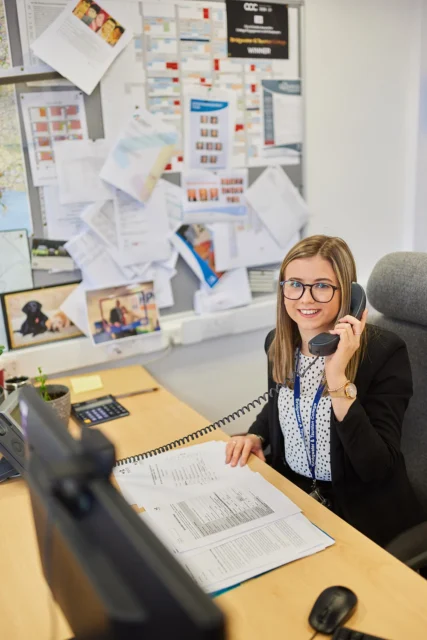 A woman sitting at a desk with a headset on, looking at papers.