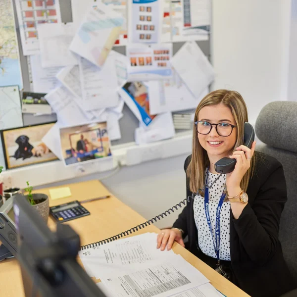 A woman sitting at a desk with a headset on, looking at papers.