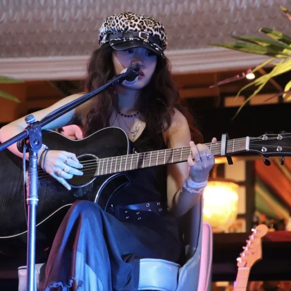 A woman wearing a tiara playing an acoustic guitar and singing into a microphone.