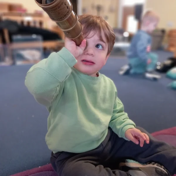 A toddler looking through a cardboard tube.