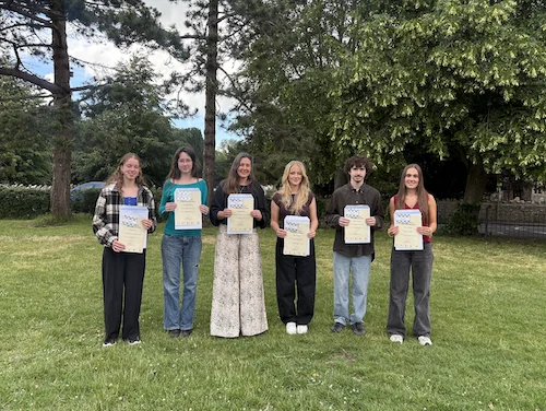 Six people holding certificates in a grassy area