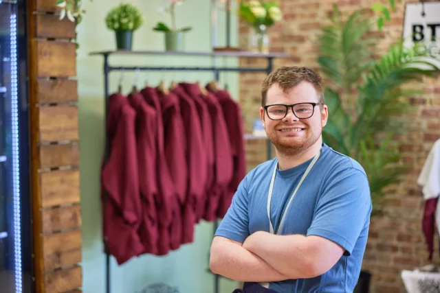 A man with short brown hair and glasses wearing a blue t-shirt with his arms crossed.