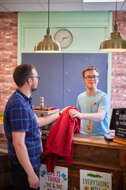 Man handing over a red garment to another man behind a counter.