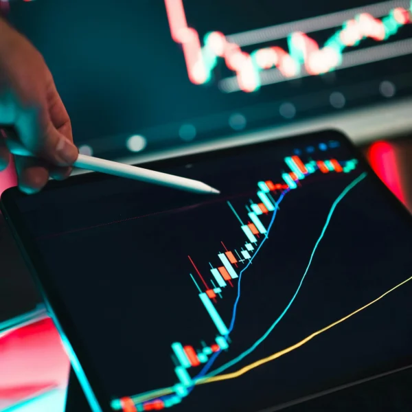 A person's hand pointing to a graph on a tablet screen with another graph visible in the background.