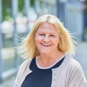 Smiling woman with blonde hair standing outside.