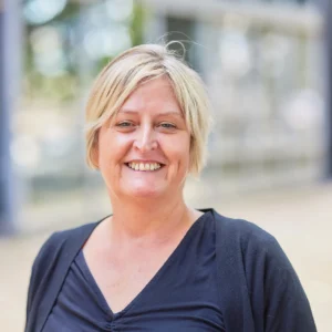 A smiling woman with short blonde hair wearing a dark blue top.