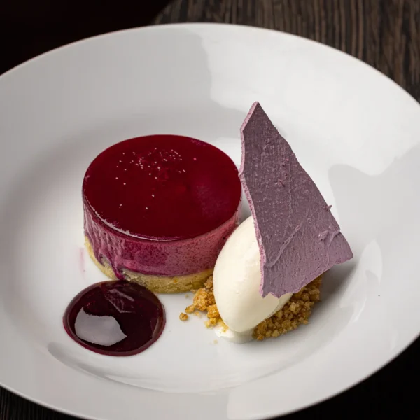 A dessert plate with a red jelly, purple chocolate and cream.