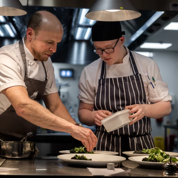 Two chefs preparing a dish in a professional kitchen. The chefs are focused on their work.