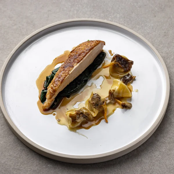 A plate with a piece of cooked fish stuffed with greens, served with brown sauce and vegetables.