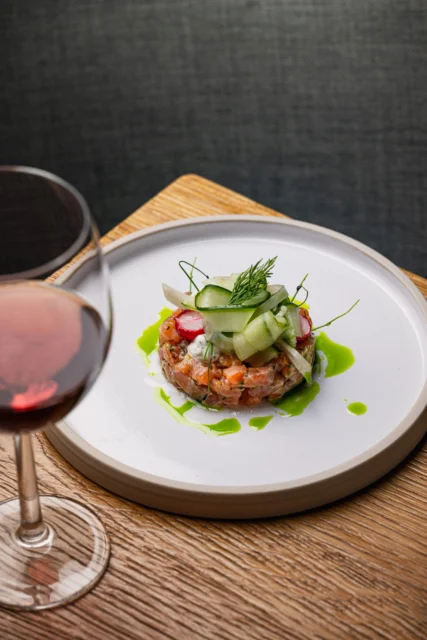 garnished dish on a white plate next to a glass of wine