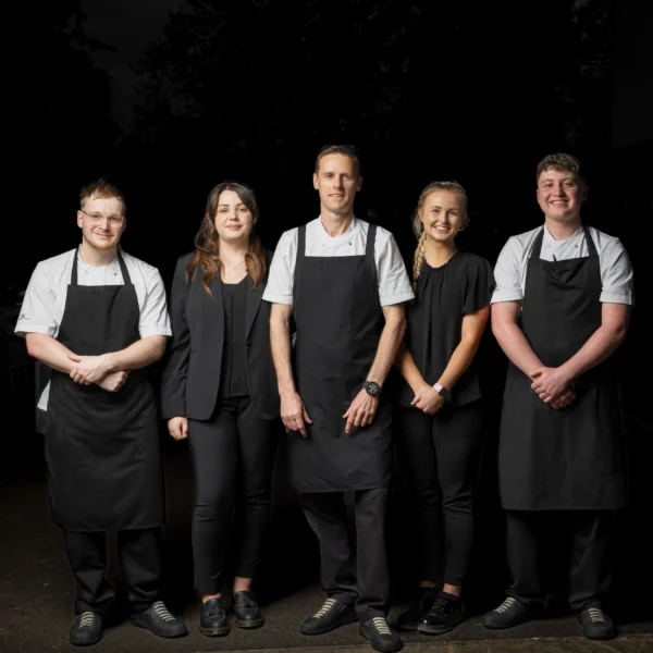 A group of five restaurant staff standing together, wearing black aprons and white shirts.