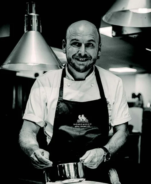 a smiling chef in a kitchen with a pot in hand