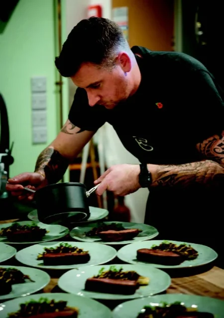 A chef garnishing a series of identical dishes