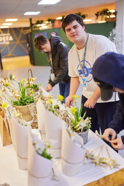 Three people preparing flower arrangements in a room with a white table.