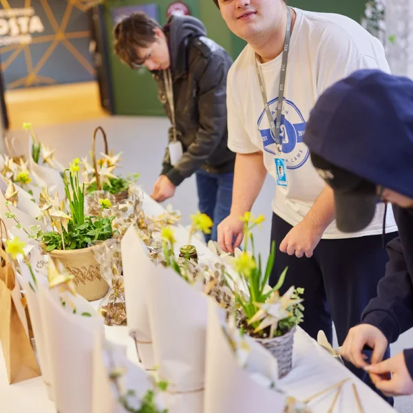 Three people preparing flower arrangements in a room with a white table.