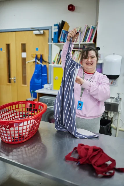 A woman standing by a metal table holding a striped dress.