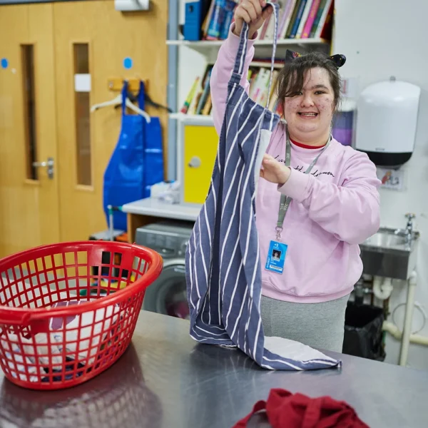 A woman standing by a metal table holding a striped dress.