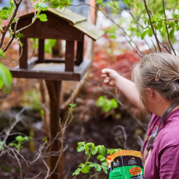 A woman feeding birds from a bird feeder in a garden.
