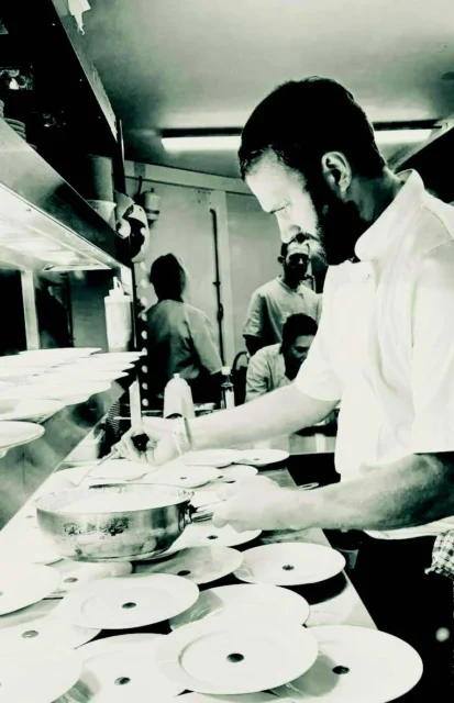 A man preparing food in a kitchen with plates on a counter.