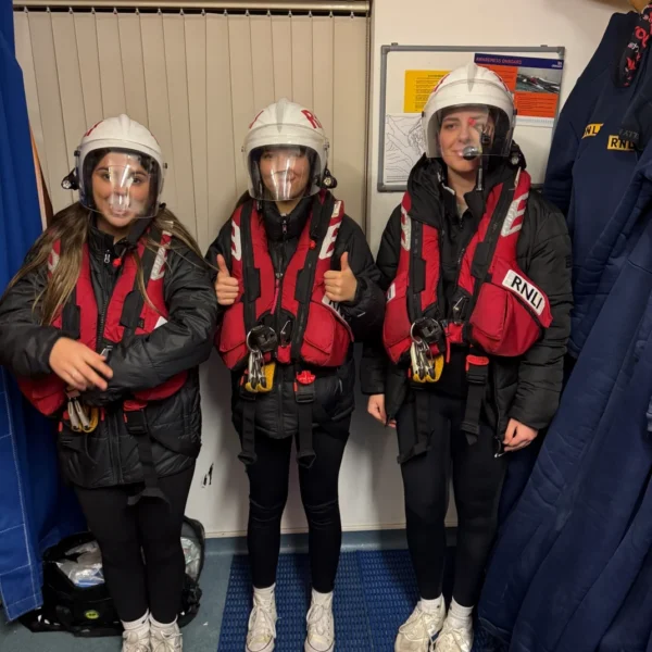 Four people wearing red and black jumpsuits and helmets standing in a line.